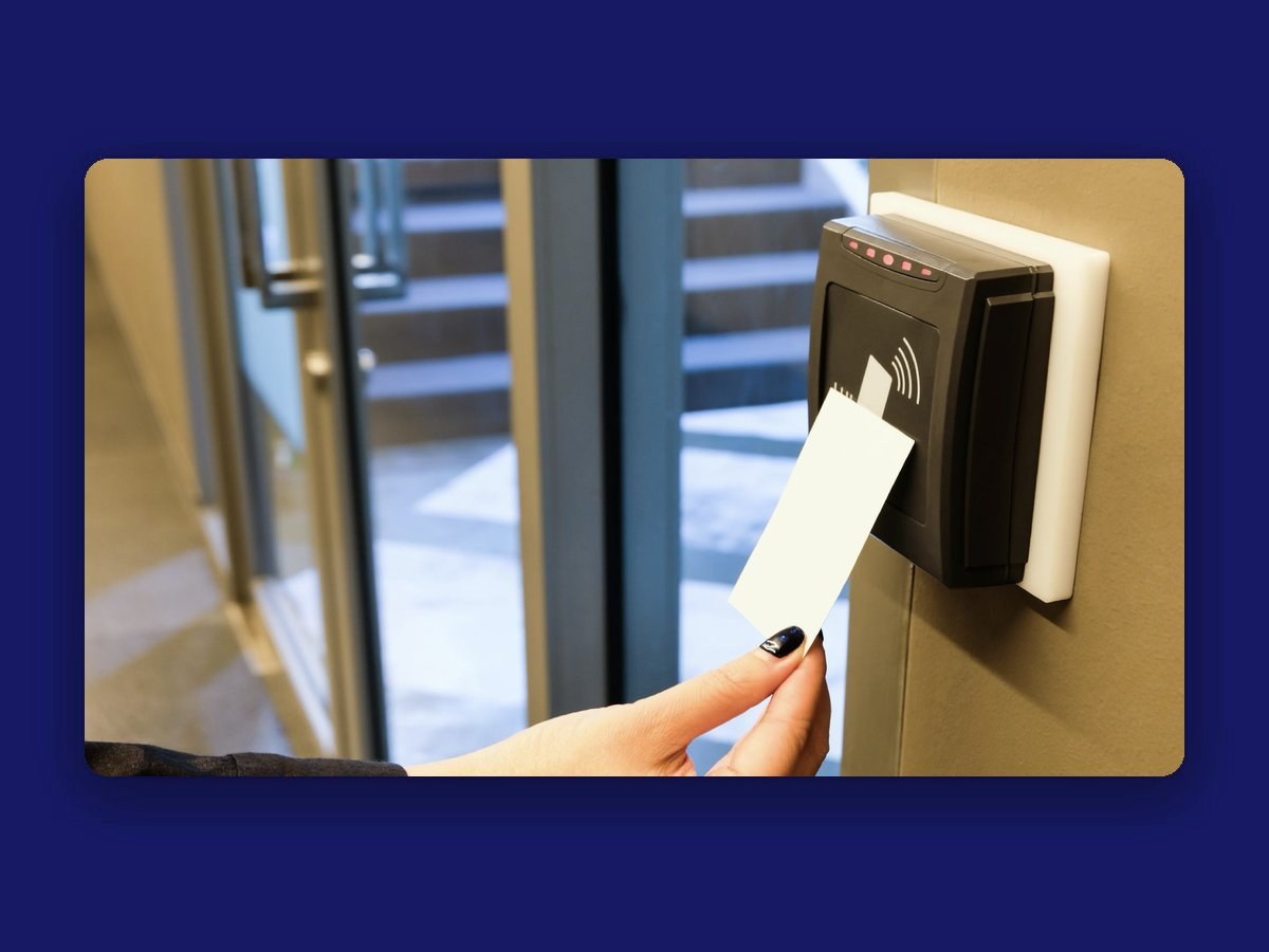A hand tapping a white keycard against a wall-mounted card reader beside a glass door